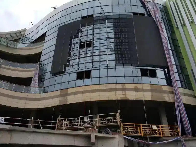 Installation process of outdoor transparent LED mesh on a curved commercial building facade, showing lightweight module mounting.