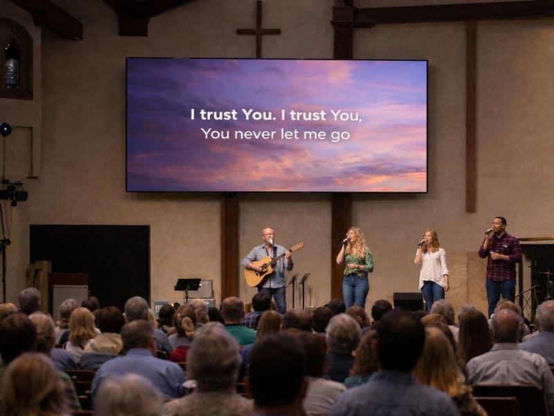 Wide-angle view of a modern church sanctuary featuring a large, bezel-less 4K LED video wall displaying worship lyrics clearly under bright stage lighting.