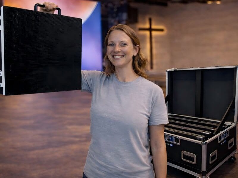 A church volunteer easily lifting a lightweight LED video wall panel from the Sunday Setup Series flight case, demonstrating fast and easy installation for mobile church events.