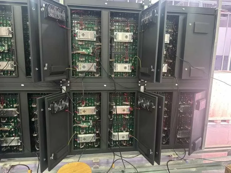 Rear view of heavy-duty iron/steel outdoor LED cabinets with double doors open. Shows internal cooling fans, power supplies, and receiving cards. Designed for permanent outdoor wall mounting and ease of rear maintenance