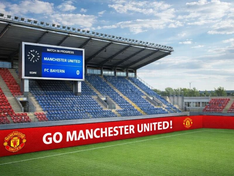 Professional football stadium equipped with a massive outdoor LED scoreboard and ground-level perimeter LED advertising banners. High refresh rate screens suitable for live sports broadcasting and fan engagement.